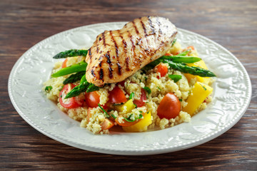 couscous salad with grilled chicken and asparagus on white plate. wooden rustic table. healthy food