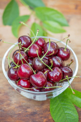Ripe red cherries with green leaves in a transparent bowl