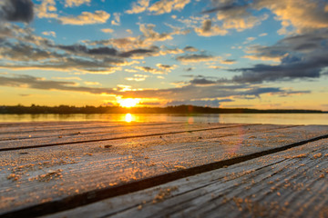 Naklejka na ściany i meble Wooden pier with water at sunset and beautiful bright clouds