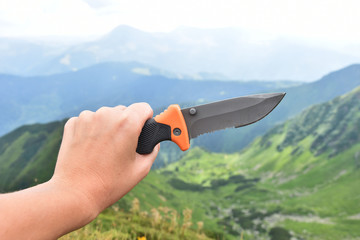Knife in hand on the background of mountains, camping knife