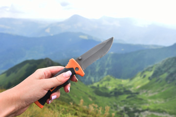 Knife in hand on the background of mountains, camping knife