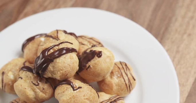 Slow motion fly out shot of profiteroles with fine dark chocolate on plate
