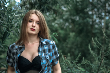 A girl with blond hair in a plaid shirt and short denim shorts on a background of trees and nature