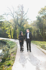 A young happy pregnant woman walks with her husband in the park and they keep hands each other