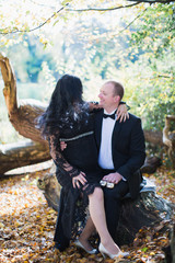 Naklejka premium A pregnant woman sits on lap of her husband who keeps a little shoes on her belly in the park and they look at each other