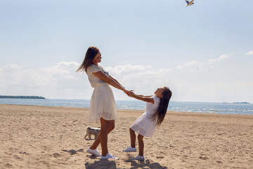 mother and daughter dressed in white fool around in dresses holding hands on sandy beach