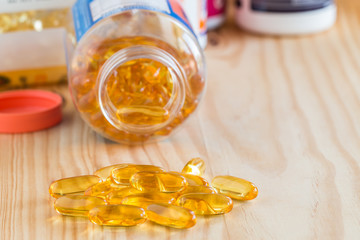 Fish oil, omega 3 with vitamin D capsules on wooden table.