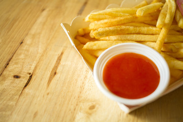 French fries and sauce in a plate of white paper on the table. on blurry background.