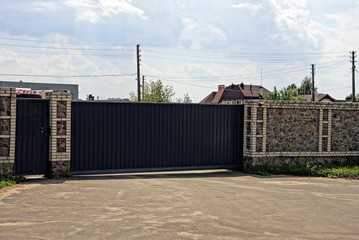 коричневые железные ворота и каменный забор у асфальтированной дороги