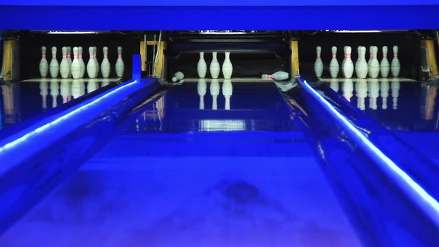 Playing bowling game on colorful alley. Bowling ball knocks down 7 pins. Process of bowling game. Bowling strike competition. Colorful Illumination. Ball is rolling on playing field