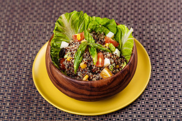 Quinoa salad with sweet corn, olive, tomato, cucumber and chives in wooden bowl