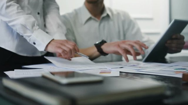 Young and smart businesspeople smiling coworking commenting and showing graphic stats, taking a business conversation in an office interior slow motion