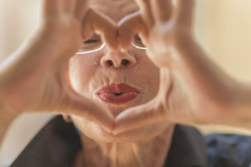 Cute senior old woman making a heart shape with her hands and fingers - 166048751