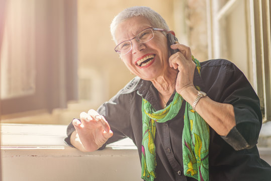 Lovely senior lady having a fun conversation with her friend or a family member over her cell phone