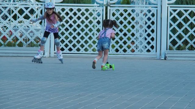 The child learns to skate. Two sisters on rollers and a scooter.