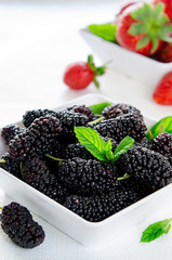 Fresh ripe mulberries and strawberries with mint in bowl on white background, copy space