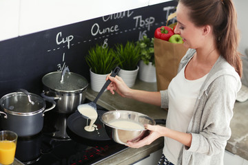 Young woman prepares pancakes in the kitchen while standing near the table. Woman in the kitchen. Cooking at kitchen.