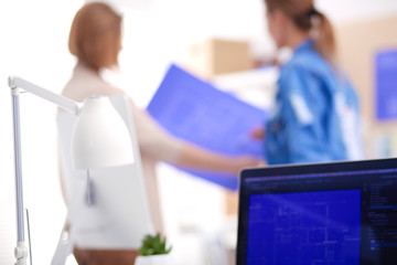 Fototapeta premium Two young woman standing near desk with instruments, plan and laptop.