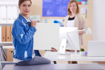 Two young woman standing near desk with instruments, plan and laptop.