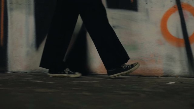 A girl wearing sneakers walks beside a spray painted wall and gradually begins running. Filmed from the ground focusing on the shoes of the model.