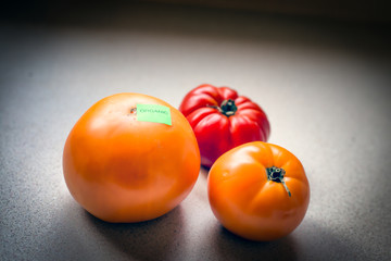 Two yellow and one red tomato on the counter; one tomato has an organic sticker on it
