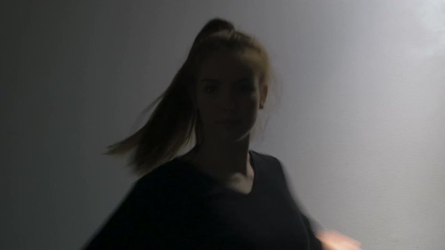 A young female dancer spins in circles in a smokey dance room. Filmed in medium close up.