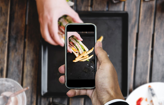 Taking food photo, food photography by smart phone, club sandwich with french fries on wooden table