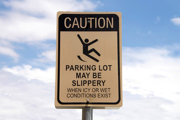Caution, Slippery when wet sign in a parking lot. Warning patrons. Blue sky with fluffy white clouds in background © sheilaf2002