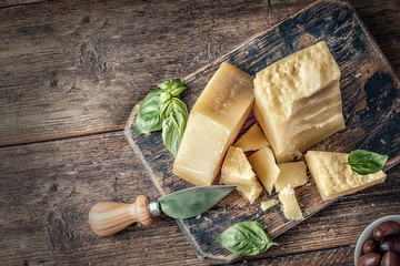 Parmesan cheese on wooden board with basil leaves. Pieces of cheese parmesan on wooden table and cheese knife. Top view. - obrazy, fototapety, plakaty