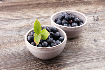 Freshly picked blueberries bowl. Juicy and fresh blueberries with green leaves on rustic table. 