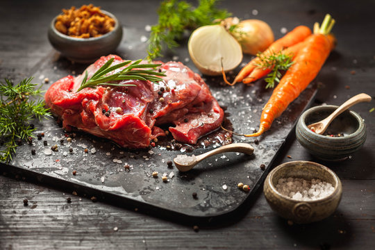 Deer or venison roast, traditional finnish food, rosvopaisti, with Chanterelle fungus, Sea salt, red, green, white pepper and coriander in clay pots on an old black rustic table. 

