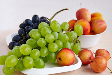 A bunch of  grapes, apples on a white plate