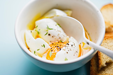 Soft boiled eggs with salt, pepper and thyme in white bowl on blue background 
