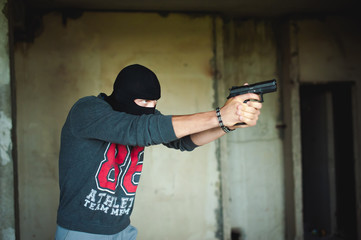 Fototapeta na wymiar Athletic man in a balaclava, holds a pistol in his hand, is threatened with shooting, aiming
