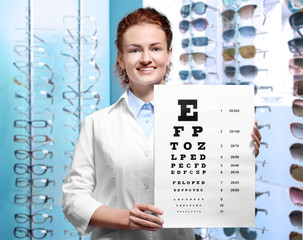 Young doctor holding eyesight test chart on grey background