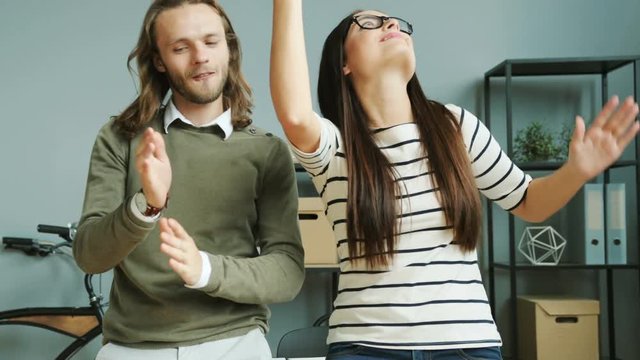 Happy beautiful business woman in the glasses and man having fun while dancing in the modern office during lunch break .
