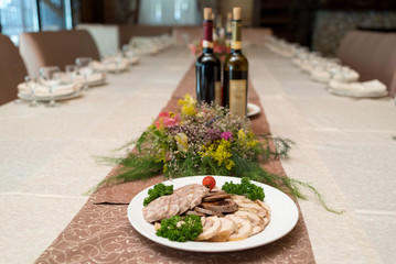 White plate with delicious sliced ham, meatloaf, tomato and parsley on celebratory dinner table in blur, selective focus. Meat platter with selection