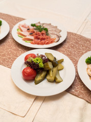 White plate with homemade pickled tomatoes, cucumbers and lettuce on celebratory dinner table. Different types of vegetables on white plate. Restaurant appetizer food