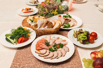 Fototapeta na wymiar Cold meat plate with delicious sliced ham, prosciutto, meat and vegetables on celebratory dinner table in blur, selective focus. Meat platter with selection on wedding banquet
