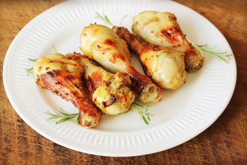 Grilled chicken legs with mustard on wooden table served on white plate with rosemary. BBQ dinner background