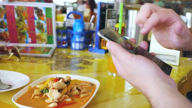 Client photographs liked the dish on a mobile phone. Take a photo of tom yam thai soup in a restaurant with mobile phone camera for social network while traveling in Thailand. 3840x2160, 4k