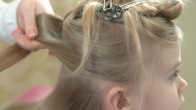 Little girl getting hair done. Hands of hairstylist working.