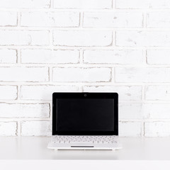 modern laptop with blank screen on the table over white brick wall