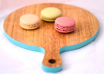 Wooden cutting board with blue border and three French macarons. Fresh colorful macaroons on chopping board. Delicious French cakes and pastries. Photo for design, menu, cafe, restaurant, web, sites.