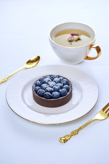 Hand made dessert tarlets from pistachio and chocolaty bakery dough with blueberry decoration served on plate with cap of tea