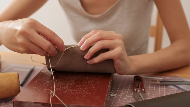 Female craftswoman sewing leather bag