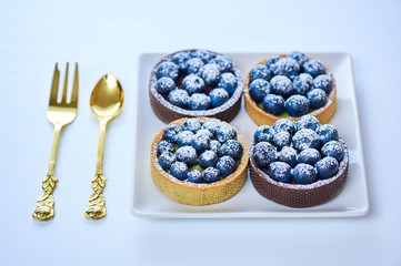 Hand made dessert tarlets from pistachio and chocolaty bakery dough with blueberry decoration served on plate with cap of tea