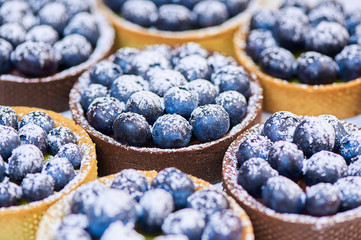 Hand made tarlets dessert from pistachio and chocolaty bakery dough with blueberry decoration on white background