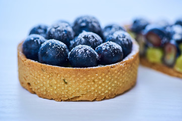 Hand made tarlets dessert from pistachio and chocolaty bakery dough with blueberry decoration on white background