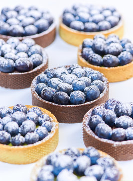 Hand made tarlets dessert from pistachio and chocolaty bakery dough with blueberry decoration on white background